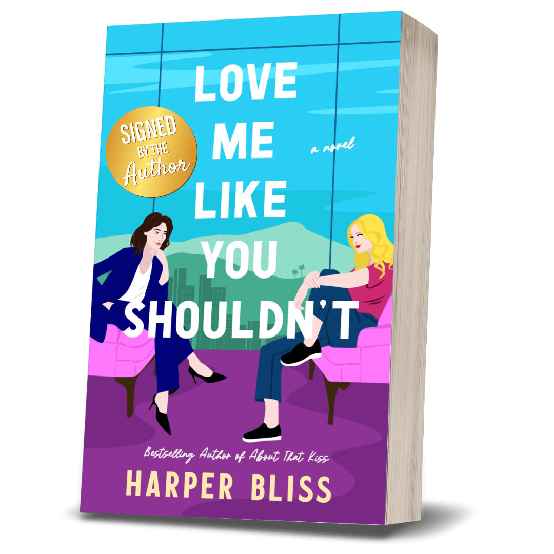 Signed paperback mockup of “Love Me Like You Shouldn’t” by Harper Bliss, with two illustrated women sitting on armchairs and a gold “Signed by the Author” sticker on the cover.